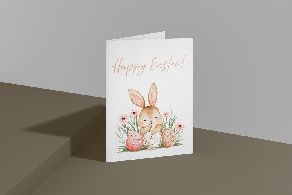 Süße Osterkarte mit einem niedlichen Hasen, der zwischen bunten Ostereiern und Frühlingsblumen sitzt. Aquarell Illustration mit sanften Pastellfarben und dem Schriftzug „Happy Easter“. Perfekt für Ostergrüße an Familie und Freunde.