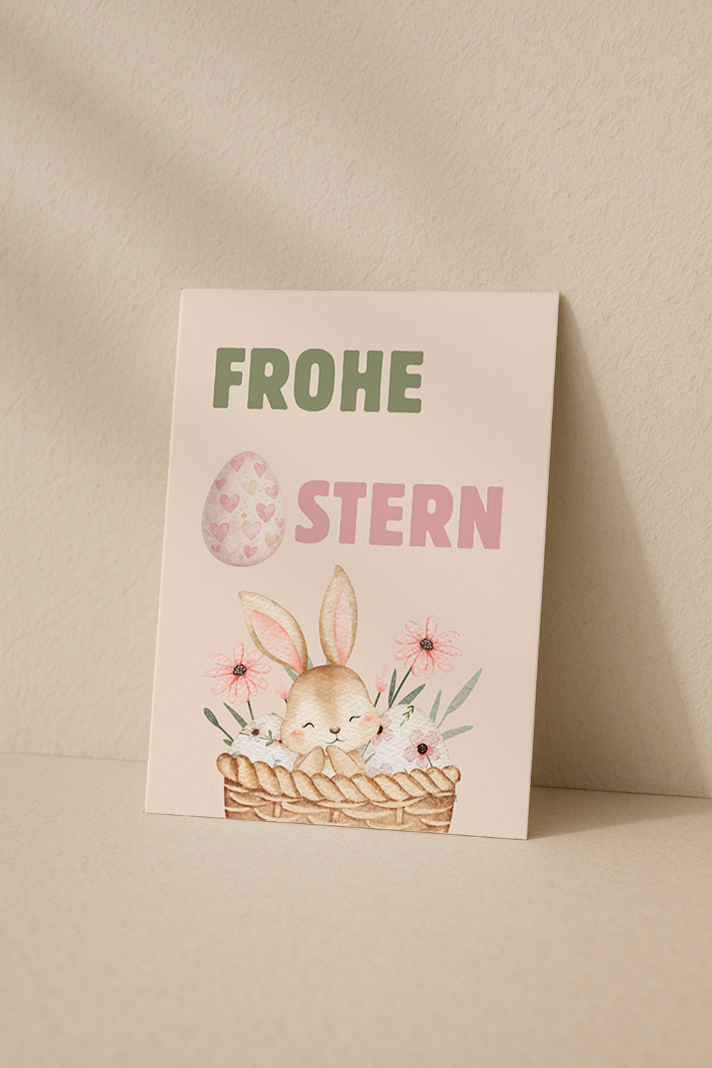 Niedliche Osterkarte mit einem kleinen Hasen in einem Korb mit Blumen und Ostereiern. Aquarell Illustration mit Pastellfarben und dem Schriftzug „Frohe Ostern“. Perfekt als Oster Grußkarte für Familie und Freunde.