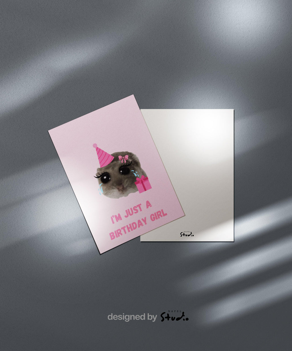 A6-Geburtstagskarte mit einem niedlichen Meme-Hamster, dessen Gesicht groß im Zentrum steht. Der Hamster trägt eine rosa Partyhut-Mütze, hat große cartoonartige Augen mit Tränen sowie lange Wimpern und eine rosa Schleife am Kopf. Daneben befindet sich ein rosa Geschenk. Unter dem Motiv steht der Spruch „I’m just a birthday girl“ in rosa Blockbuchstaben. Das Design ist humorvoll, verspielt und trendy und eignet sich perfekt als witzige Karte für Mädchen oder Meme-Fans.