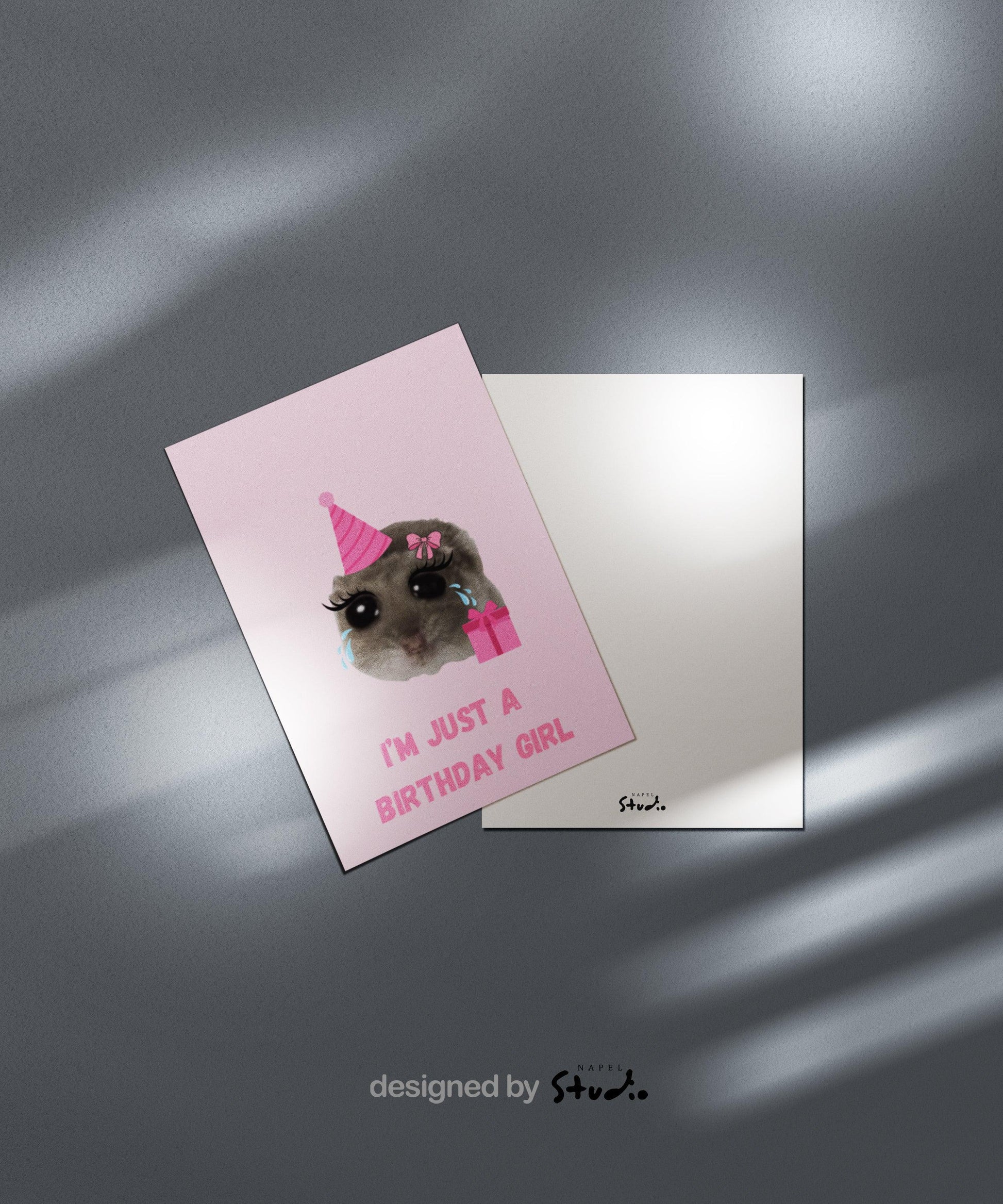 A6-Geburtstagskarte mit einem niedlichen Meme-Hamster, dessen Gesicht groß im Zentrum steht. Der Hamster trägt eine rosa Partyhut-Mütze, hat große cartoonartige Augen mit Tränen sowie lange Wimpern und eine rosa Schleife am Kopf. Daneben befindet sich ein rosa Geschenk. Unter dem Motiv steht der Spruch „I’m just a birthday girl“ in rosa Blockbuchstaben. Das Design ist humorvoll, verspielt und trendy und eignet sich perfekt als witzige Karte für Mädchen oder Meme-Fans.