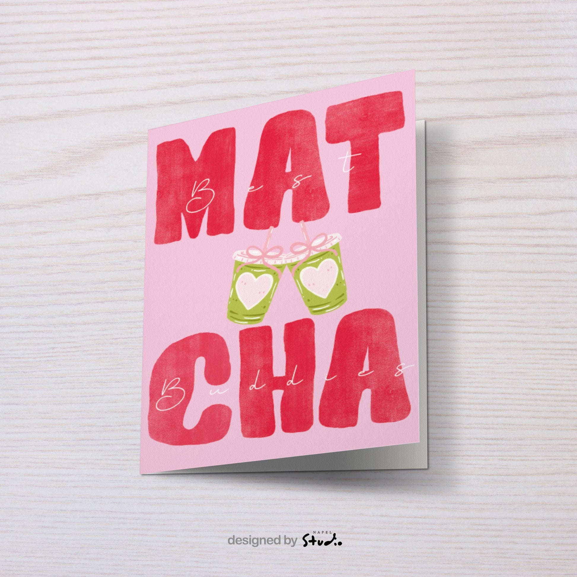 A6 Grußkarte mit rosa Hintergrund und großem roten Typografie-Text „MATCHA“. Dazwischen steht in feiner Handschrift „Best Buddies“. In der Mitte zwei gezeichnete Matcha-Becher mit Herzen, die anstoßen. Süßes, modernes Design ideal für Freundschaft, Geschenke und Matcha-Fans.