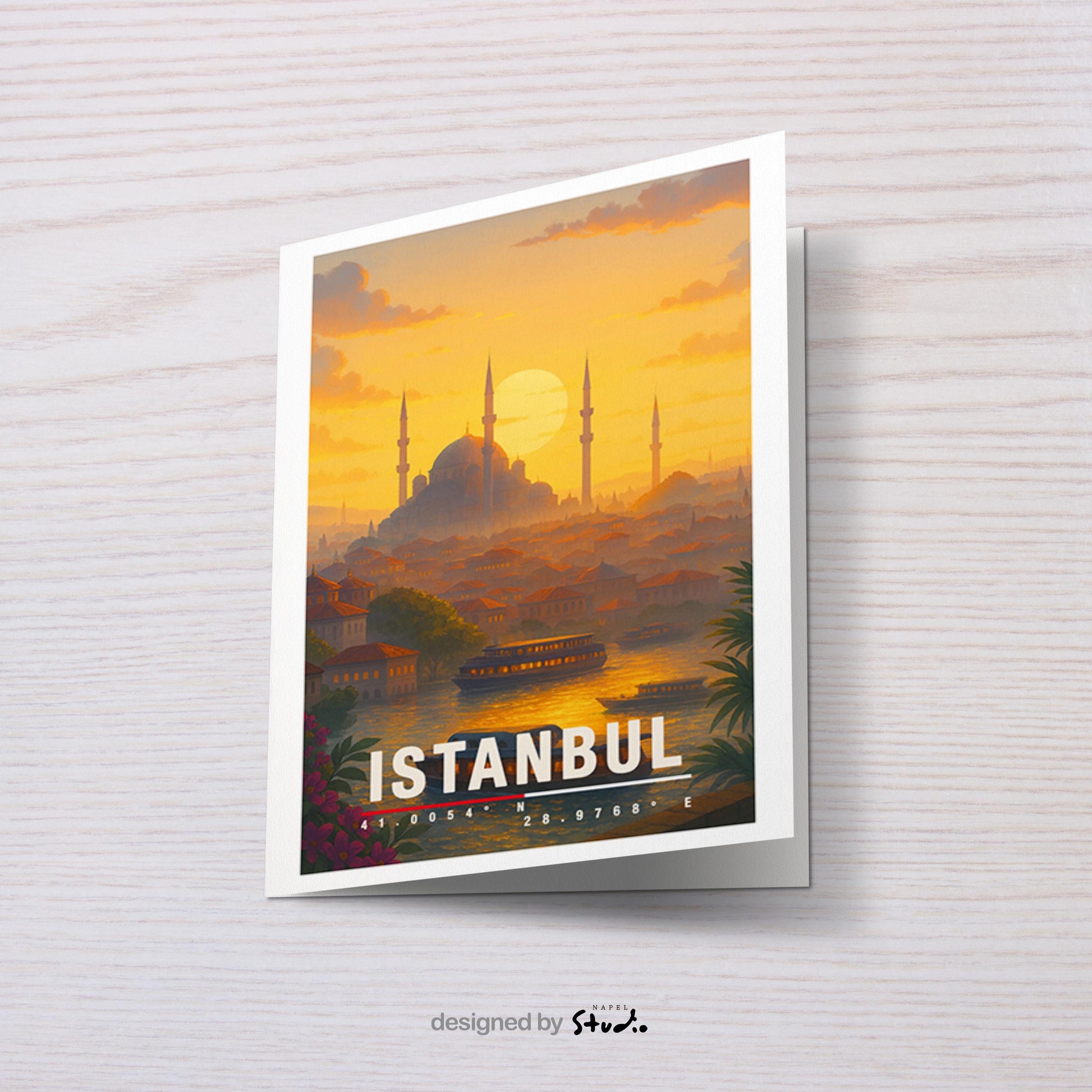 A6 Grußkarte mit Istanbul-Illustration bei warmem Sonnenuntergang. Im Vordergrund Wasser mit Booten, dahinter Häuser und die Silhouette einer großen Moschee mit Minaretten. Unten steht „Istanbul“ mit Koordinaten. Stimmungsvolle Reisekarte als Geschenk für Türkei-Fans.