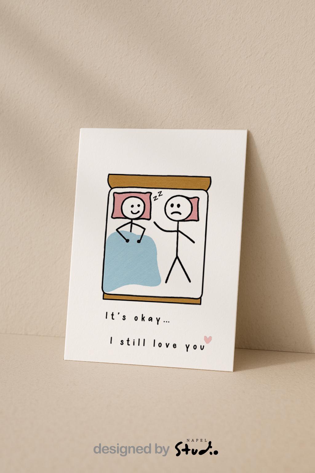 A6-Liebeskarte mit zwei Strichmännchen im Bett: eine Figur schläft lächelnd, die andere liegt wach und wirkt traurig. Darunter steht „It’s okay… I still love you“. Sanfte, humorvolle Illustration über Liebe, Nähe und Beziehungsmomente. Zartes, minimalistisches Design.