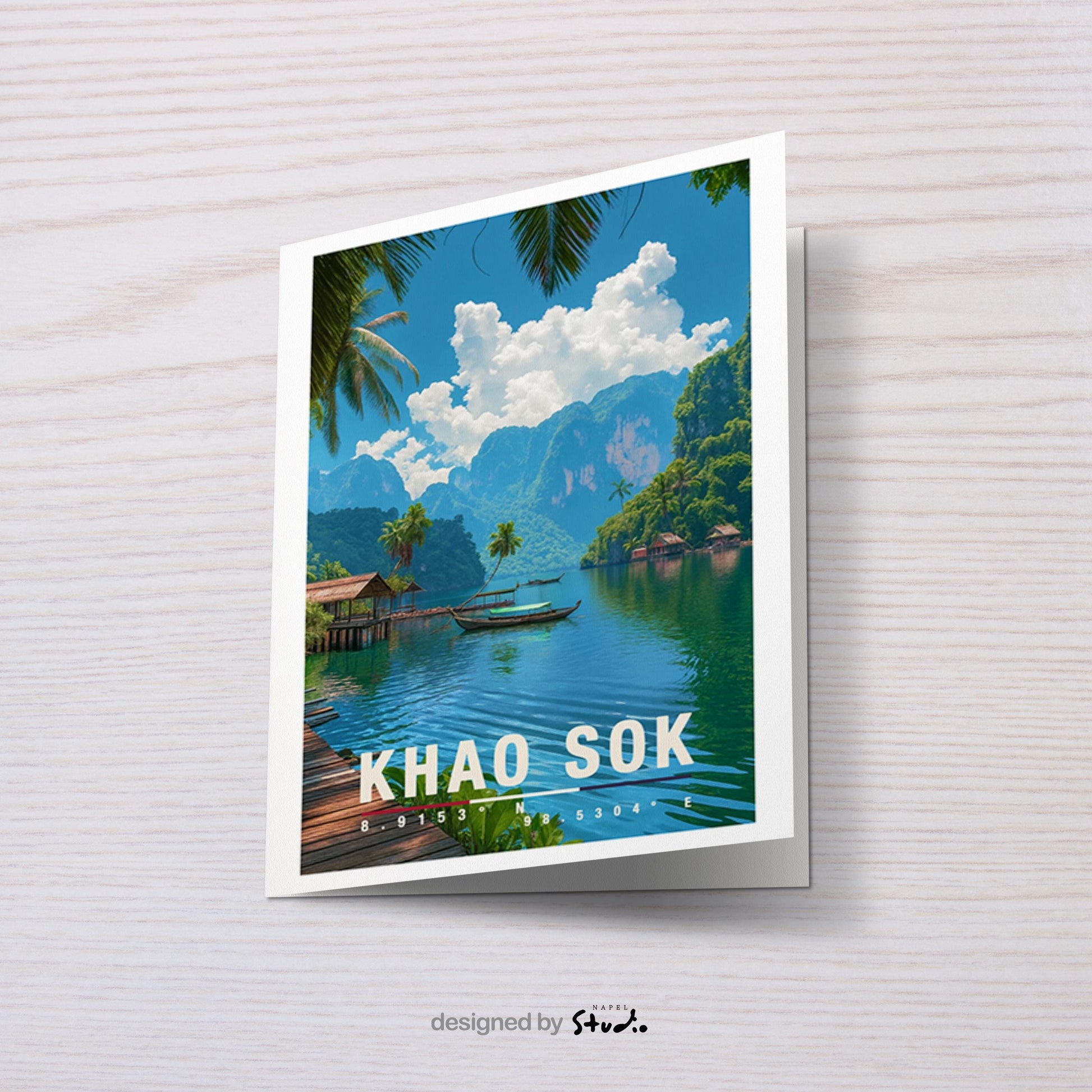 A6-Grußkarte mit Khao-Sok-Illustration: Tropischer See mit türkisgrünem Wasser, Holzbungalows am Ufer und einem Boot in der Mitte. Umgeben von Palmen, dichter Vegetation und hohen Kalksteinfelsen unter blauem Himmel mit Wolken. Moderner Travel-Poster-Stil, ideal als Reise- oder Souvenirkarte für Thailand- und Natur-Liebhaber.