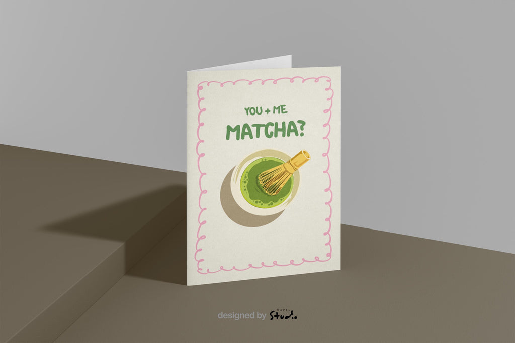 A6 Grußkarte mit heller cremefarbener Fläche und rosa Rahmen. Oben steht der Text „You + Me Matcha?“ in grüner Schrift. Darunter eine Illustration einer Matcha-Schale mit Bambusbesen. Süßes, verspieltes Design für Partner, Freundschaft oder Matcha-Fans.