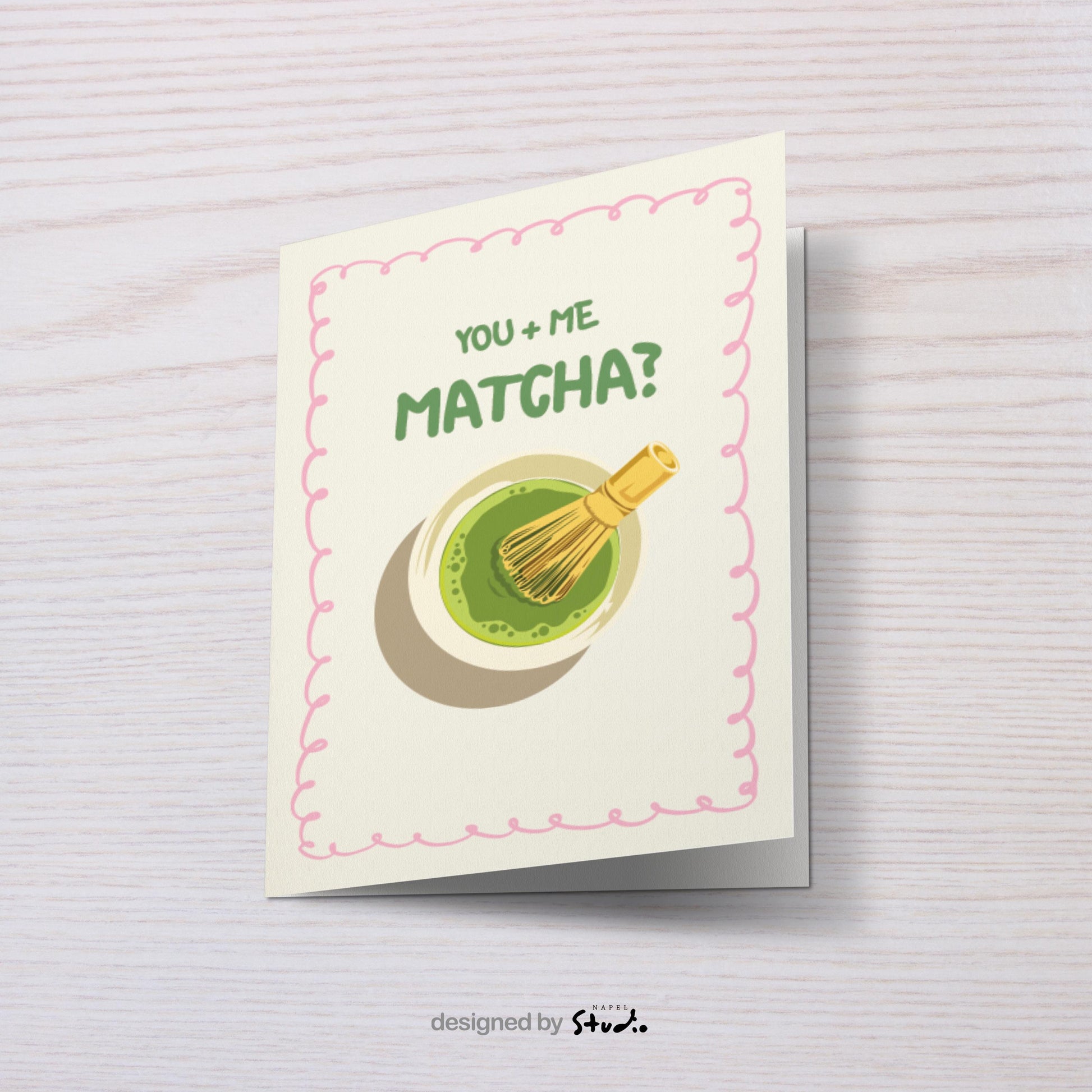 A6 Grußkarte mit heller cremefarbener Fläche und rosa Rahmen. Oben steht der Text „You + Me Matcha?“ in grüner Schrift. Darunter eine Illustration einer Matcha-Schale mit Bambusbesen. Süßes, verspieltes Design für Partner, Freundschaft oder Matcha-Fans.