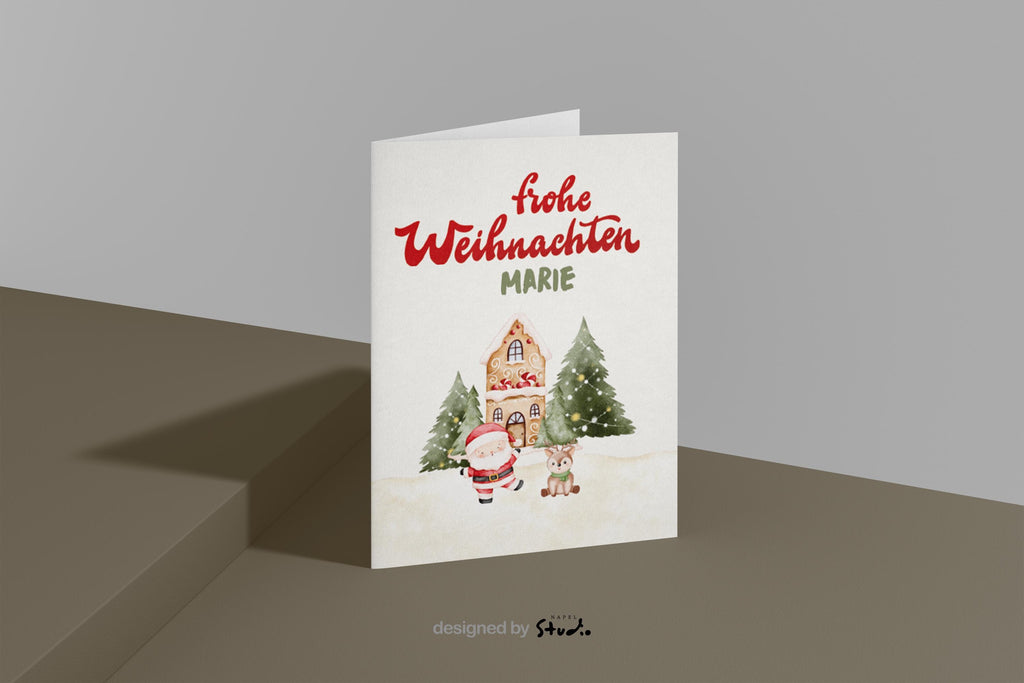 A6 Weihnachtskarte mit hellbeigem Hintergrund und roter Schrift „Frohe Weihnachten“. Darunter der personalisierte Name „Marie“. Unten steht ein gezeichneter Weihnachtsmann neben einem kleinen Reh vor einem Lebkuchenhaus und zwei geschmückten Tannenbäumen. Süße, warme Illustration für Kinder, Familie und personalisierte Weihnachtsgrüße.