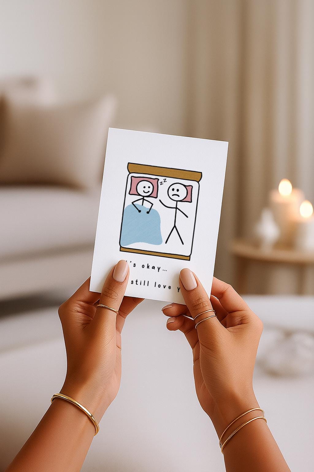 A6-Liebeskarte mit zwei Strichmännchen im Bett: eine Figur schläft lächelnd, die andere liegt wach und wirkt traurig. Darunter steht „It’s okay… I still love you“. Sanfte, humorvolle Illustration über Liebe, Nähe und Beziehungsmomente. Zartes, minimalistisches Design.