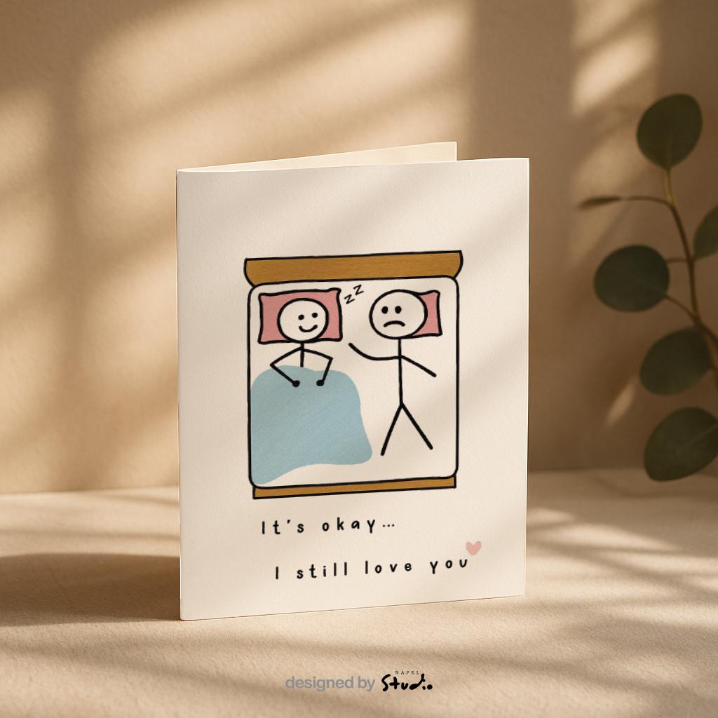 A6-Liebeskarte mit zwei Strichmännchen im Bett: eine Figur schläft lächelnd, die andere liegt wach und wirkt traurig. Darunter steht „It’s okay… I still love you“. Sanfte, humorvolle Illustration über Liebe, Nähe und Beziehungsmomente. Zartes, minimalistisches Design.