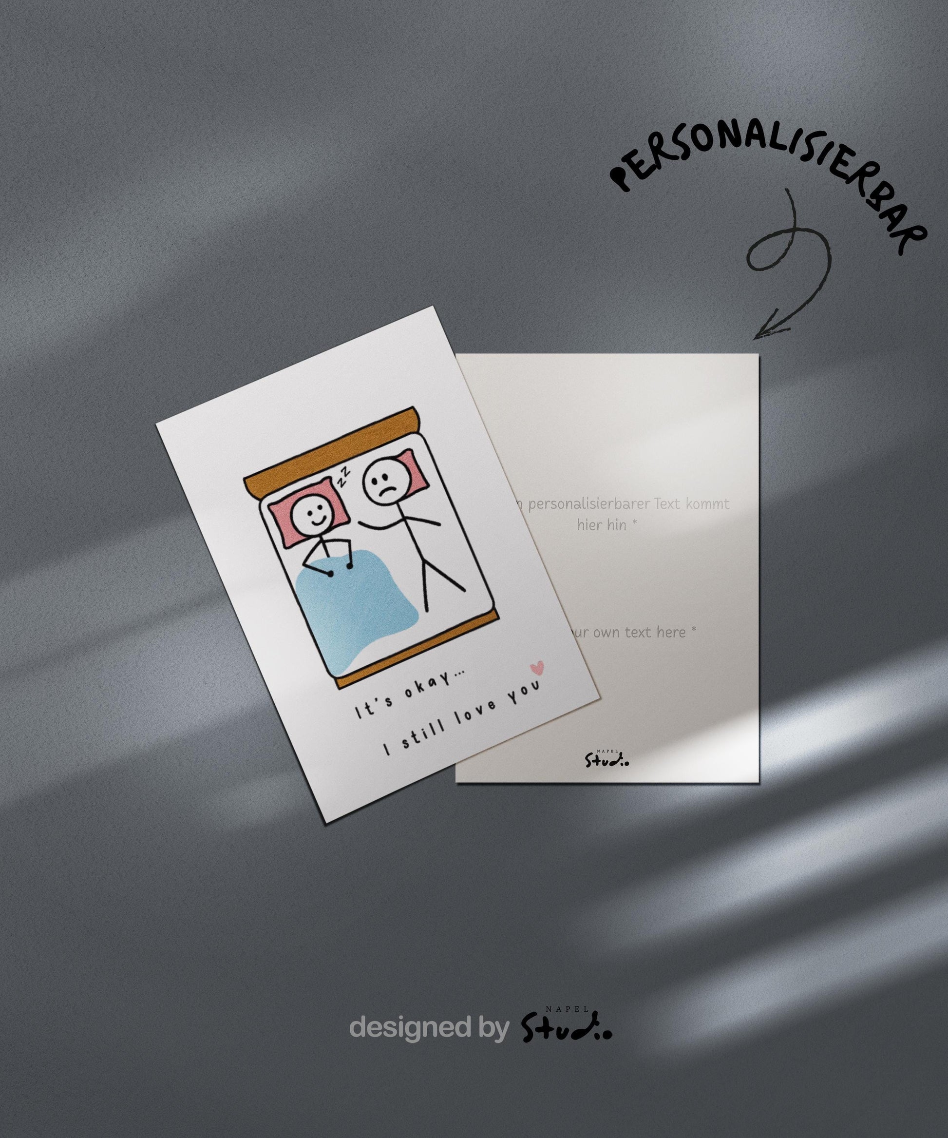 A6-Liebeskarte mit zwei Strichmännchen im Bett: eine Figur schläft lächelnd, die andere liegt wach und wirkt traurig. Darunter steht „It’s okay… I still love you“. Sanfte, humorvolle Illustration über Liebe, Nähe und Beziehungsmomente. Zartes, minimalistisches Design.