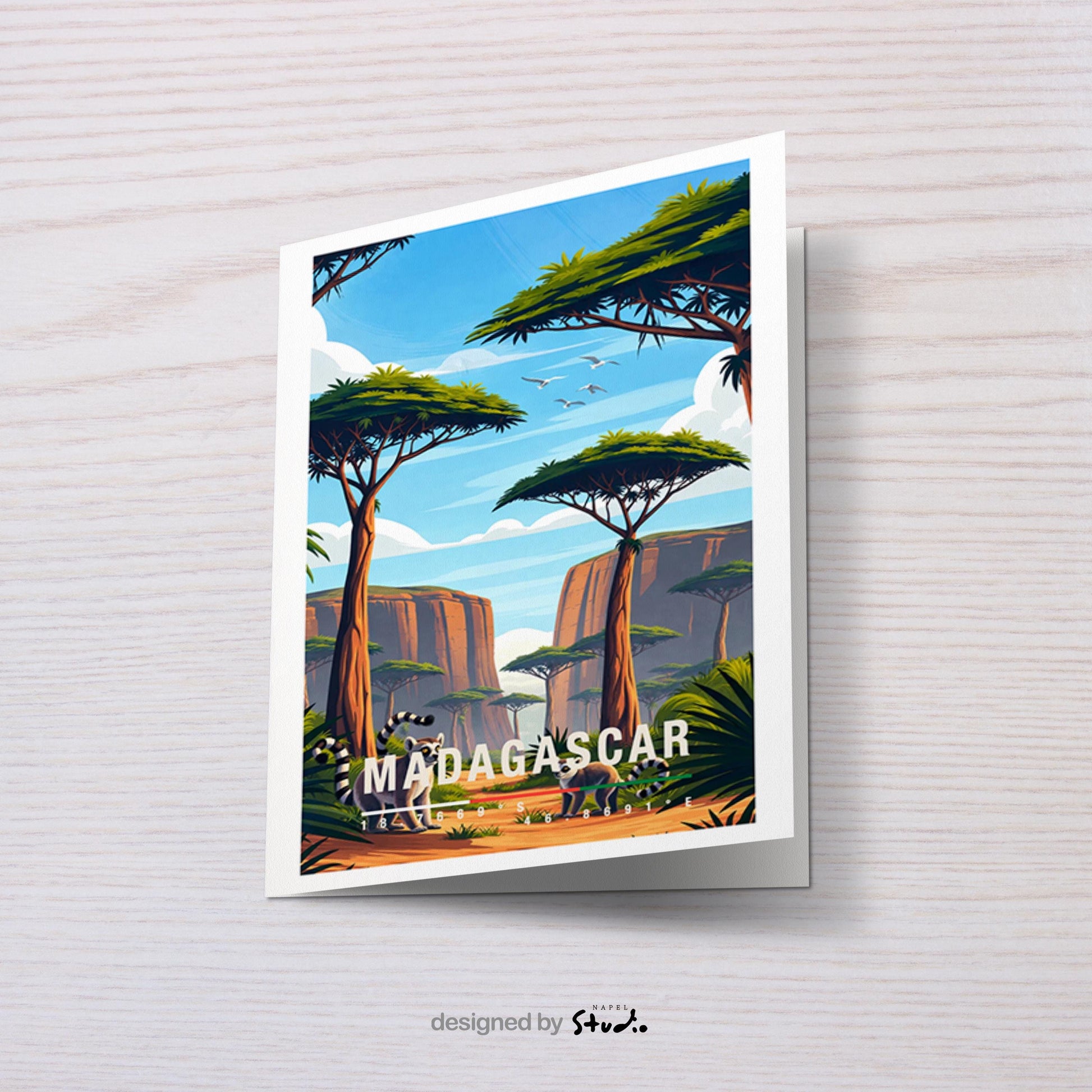 Illustrative Grußkarte mit einer warmen, farbenfrohen Landschaft aus Madagaskar. Im Vordergrund stehen zwei Lemuren auf einem sandfarbenen Pfad, umgeben von üppigem Grün und typischen Pflanzen. Hohe, charakteristische Bäume mit flachen Kronen prägen die Szenerie, während sich im Hintergrund felsige Schluchten und eine weite Naturkulisse unter blauem Himmel mit sanften Wolken erstrecken. Fliegende Vögel verleihen dem Motiv Leichtigkeit und Tiefe. Die Karte vermittelt Abenteuer, Exotik.